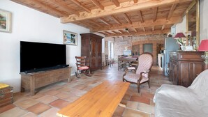 A spacious living room with a wooden ceiling, a television, a dining area, and a fireplace. - Gîte du petit Bigot – Tranquility and Nature at the Foot of the Pyrenees (Saverdun)
