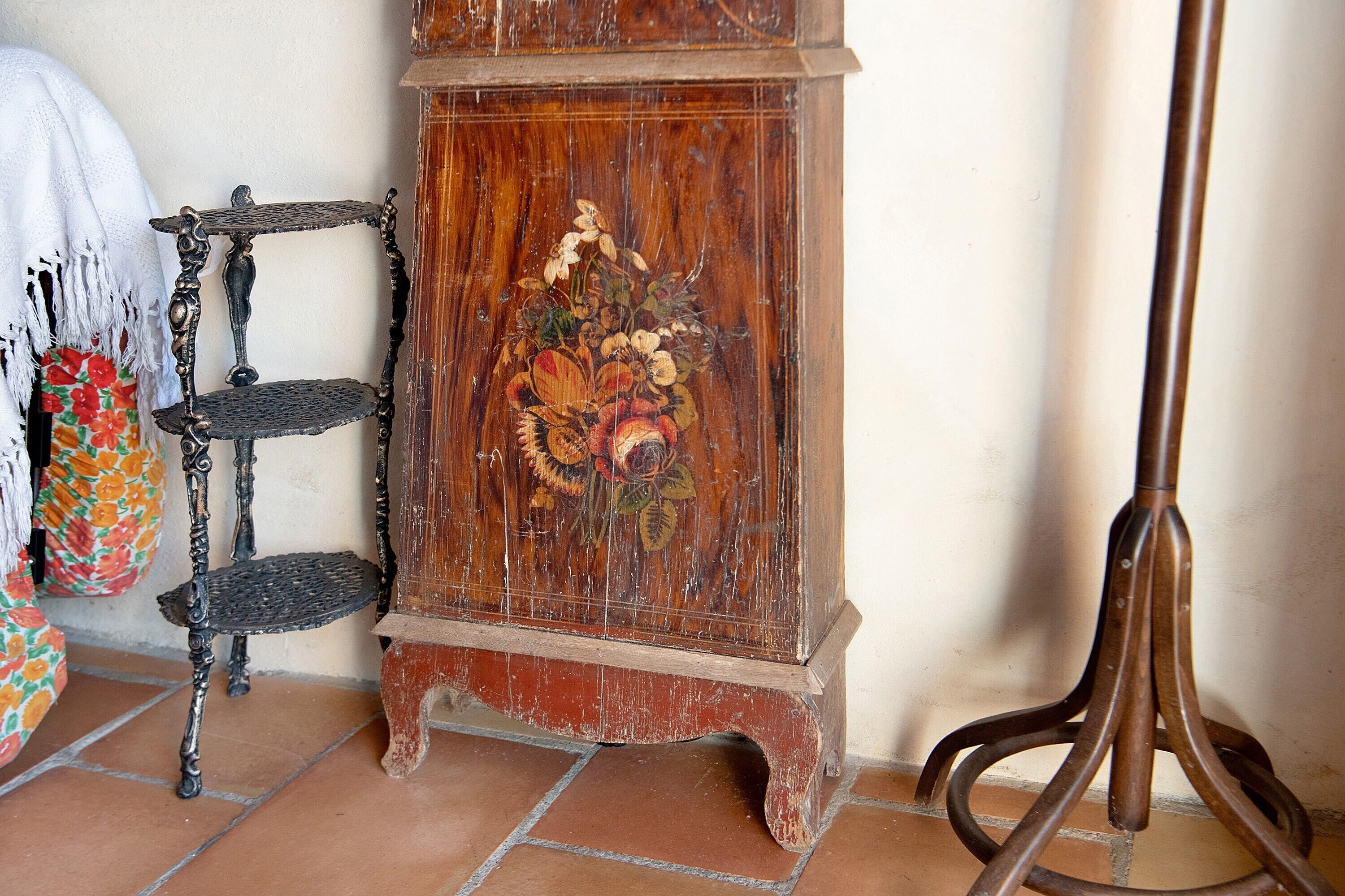 A wooden cabinet with floral artwork, a metal shelf, and a floor lamp.