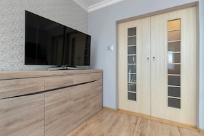 A room with a wooden cabinet, a flat-screen TV, and a wooden wardrobe with glass doors. - Bright Apartment with Balcony | Close to Old Town (Gdańsk)