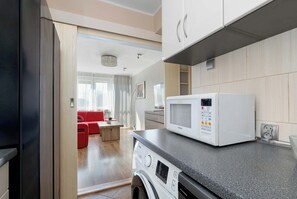A modern kitchen with a microwave, washing machine, and a red sofa in the living area. - Bright Apartment with Balcony | Close to Old Town (Gdańsk)