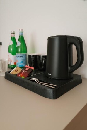 Een zwarte mok, twee groene flessen, een glas en een dienblad met bestek op een aanrecht.