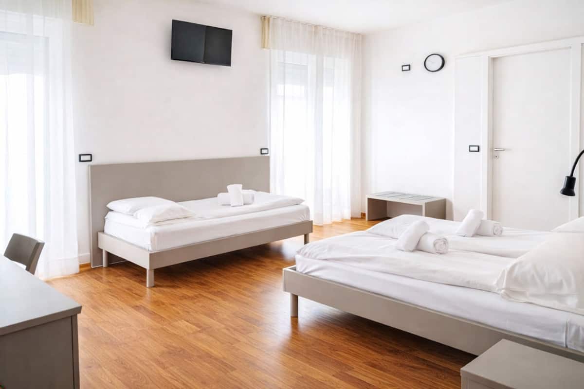 A hotel room with two beds, a desk, a TV mounted on the wall, and a door with a handle.