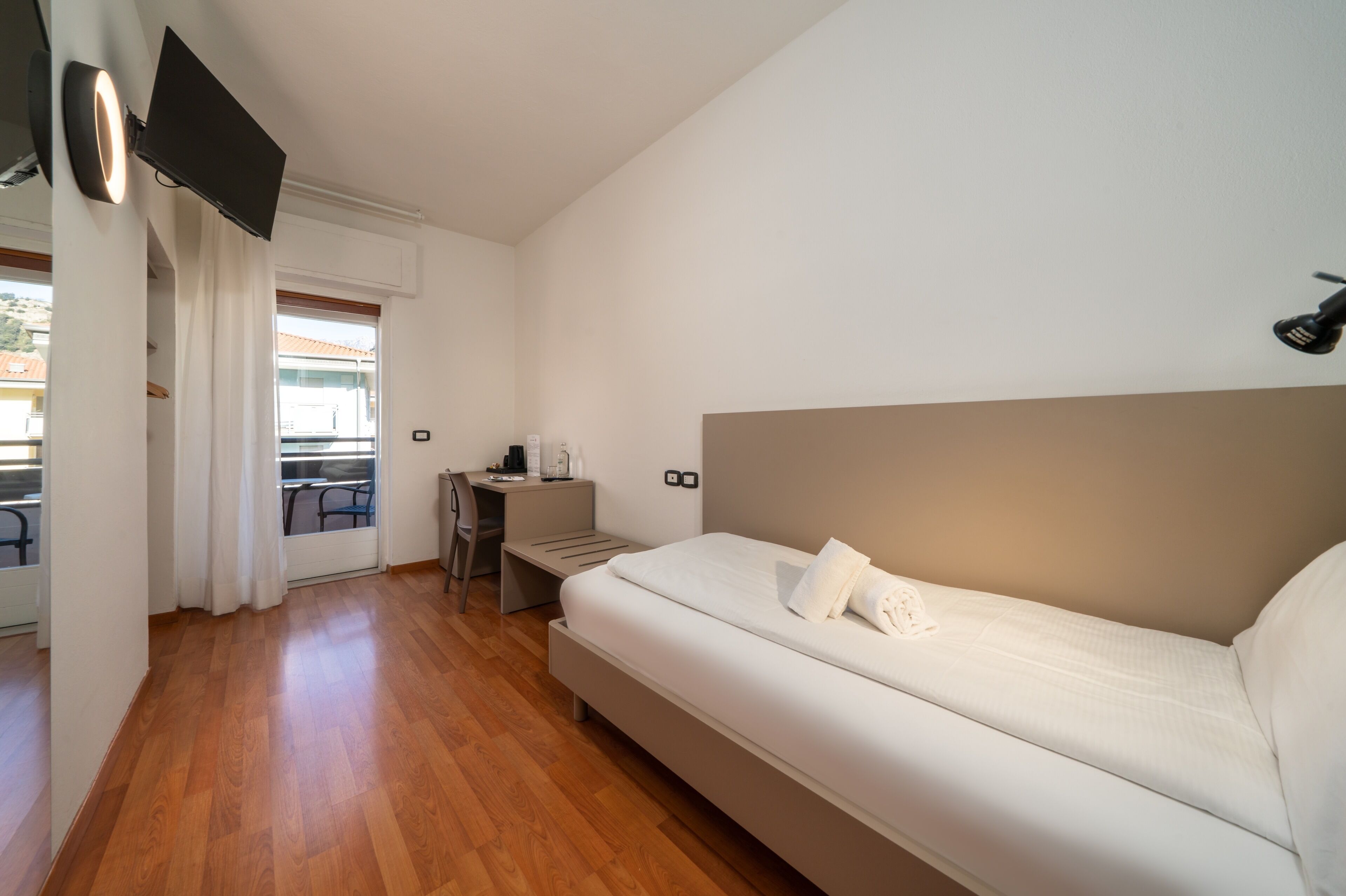 A bedroom with a bed, a desk, a chair, a TV mounted on the wall, and a window with curtains.