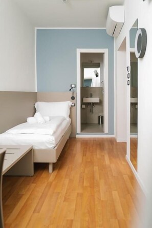 Een moderne hotelkamer met een houten vloer, een bed met witte lakens, een bureau en een badkamer door een open deur zichtbaar.
