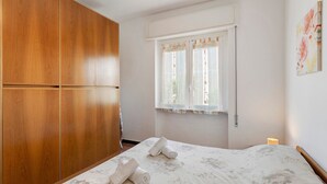 Un dormitorio con cama, un armario de madera, una ventana con cortinas y una lámpara fijada a la pared.