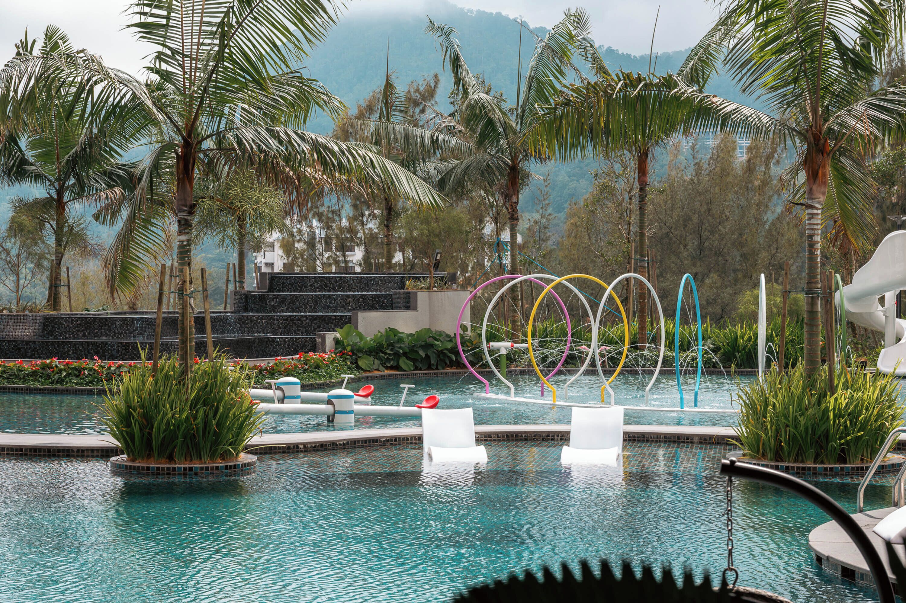 A pool area with lounge chairs, a water feature, and palm trees.