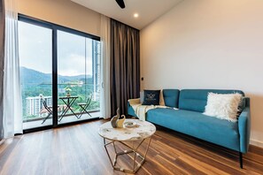 A modern living room with a blue sofa, a round coffee table, and a view of a cityscape through large windows. - Antharas 1 Premier Suites Genting (Genting Highlands)