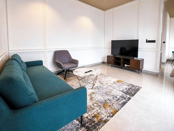 A modern living room with a teal sofa, a grey armchair, a coffee table, and a flat-screen TV on a wooden stand. - Antharas 1 Premier Suites Genting (Genting Highlands)