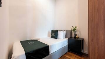 Une chambre à coucher bien rangée, avec un lit, une table de chevet ornée d’un vase et une armoire en bois.