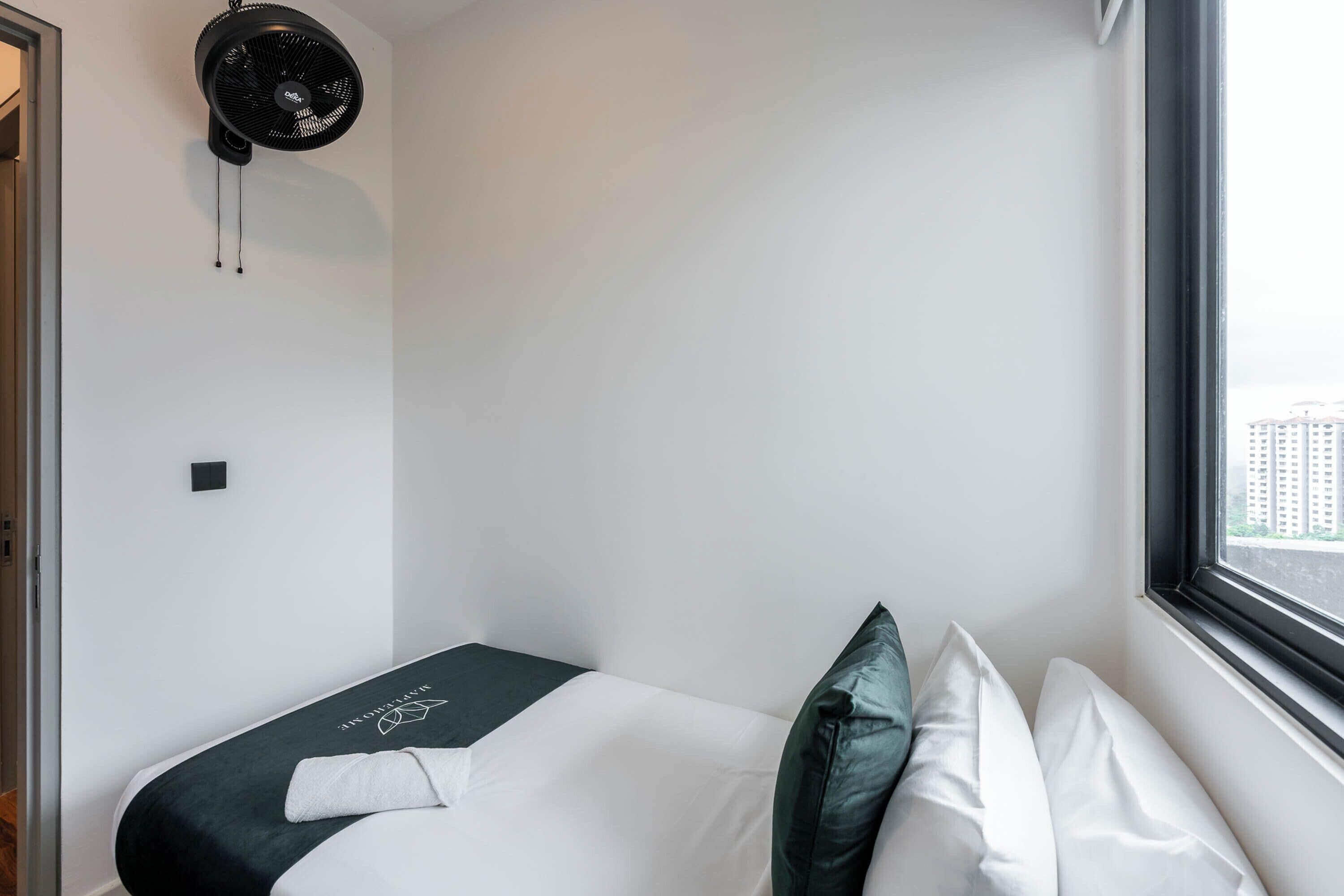 A hotel room with a bed, a window, and a wall-mounted fan.