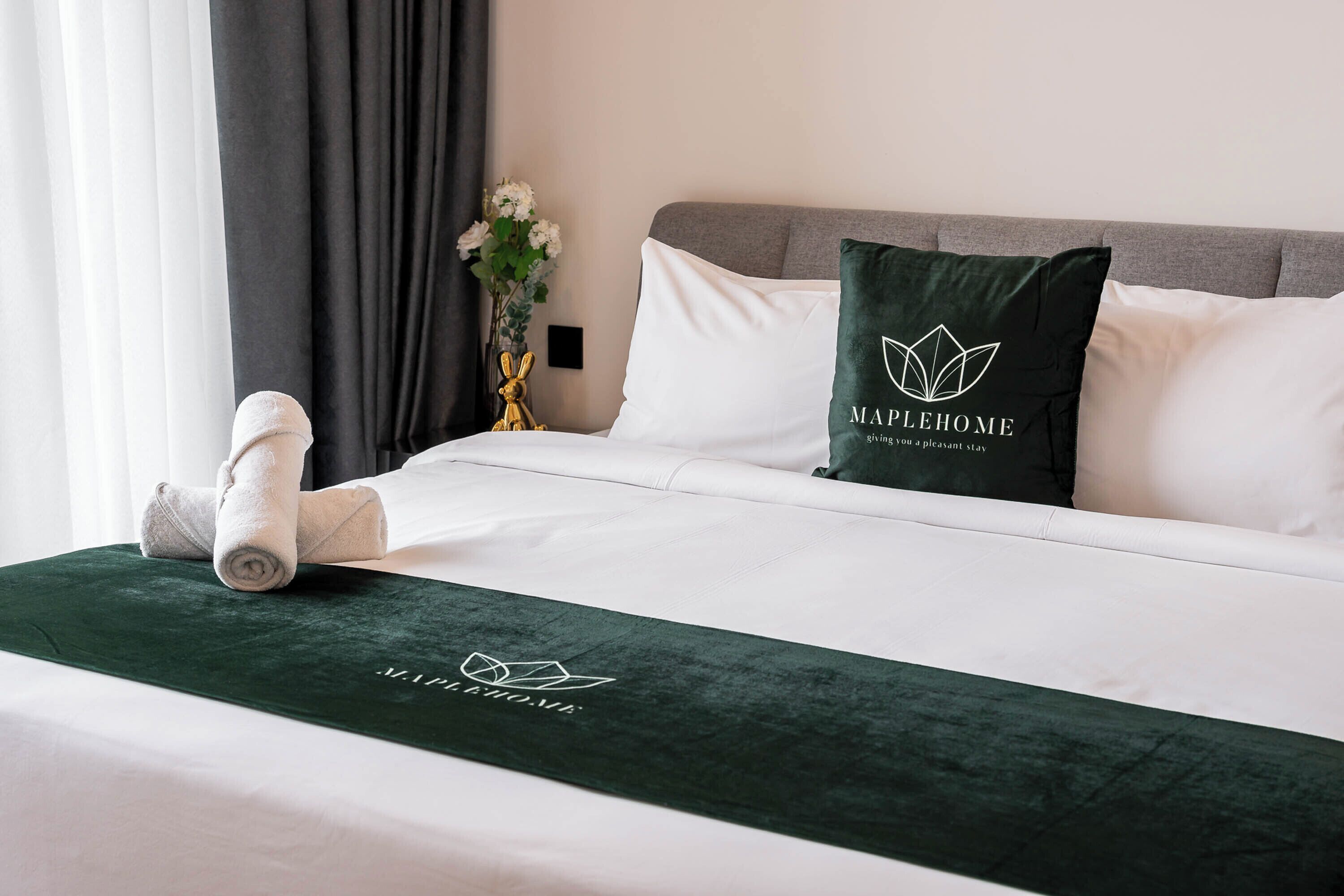 A neatly made bed with a green bedspread, white pillows, and a pillow with a logo.
