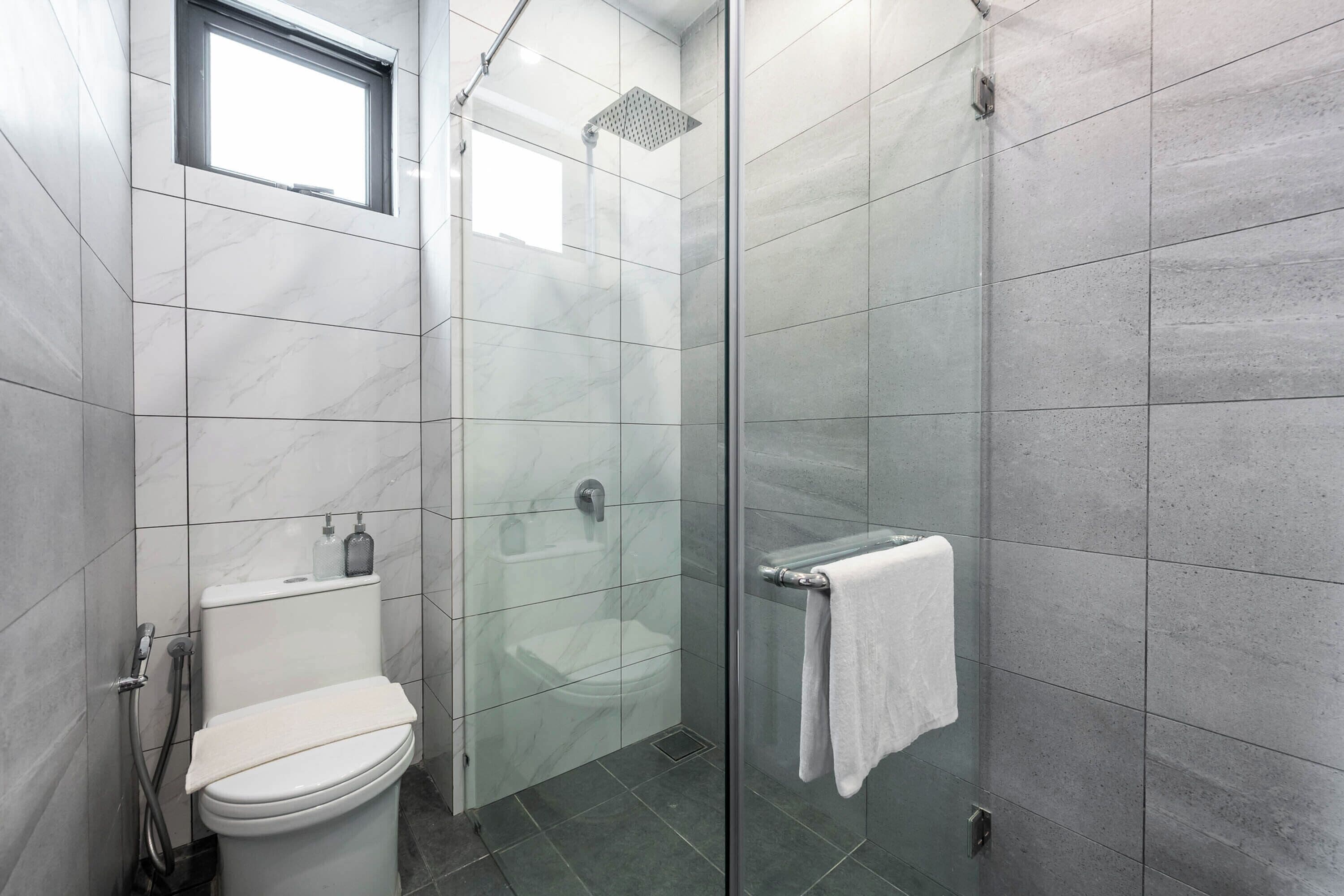 Un baño moderno con inodoro, ducha con puerta de vidrio y barra para toallas.