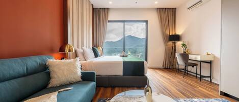 A hotel room with a bed, a sofa, a desk, and a view of a mountain.