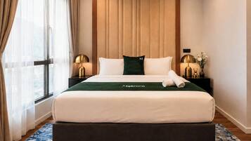 Habitación de hotel con cama, mesita de noche, lámpara, ventana con cortinas y vistas al exterior.