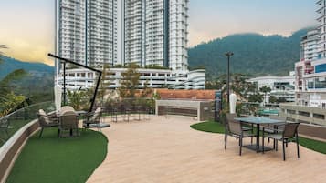 A rooftop patio with outdoor furniture, a pool, and high-rise buildings in the background.