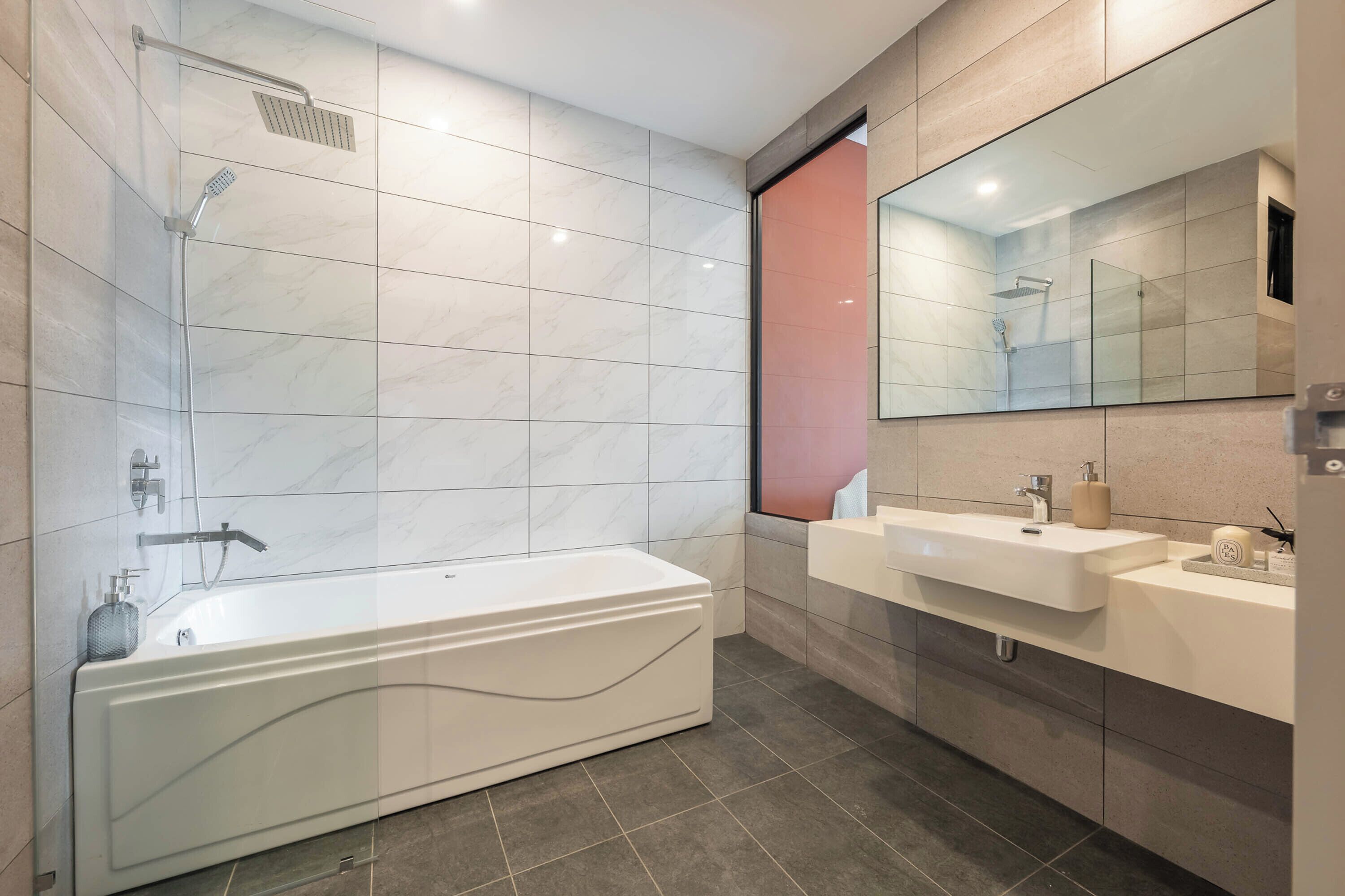 A modern bathroom with a freestanding bathtub, a large mirror, and two sinks.