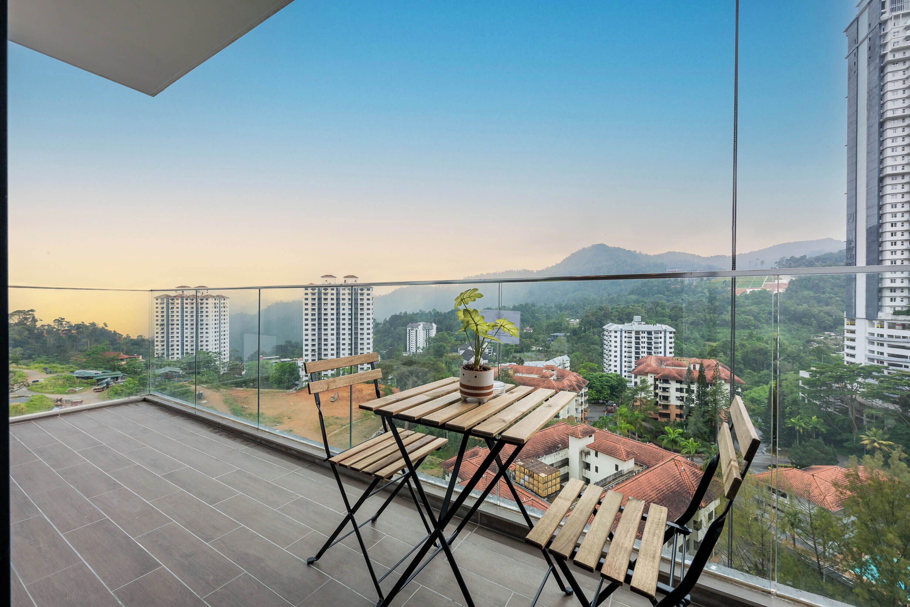 A balcony with a wooden table and chairs, a potted plant, and a view of surrounding buildings and greenery.