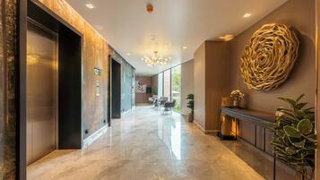 A modern hotel lobby with a marble floor, elevators, a reception desk, and a large decorative wall piece.