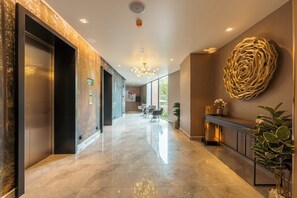 A modern hotel lobby with a marble floor, elevators, a reception desk, and a large decorative wall piece. - Antharas 1 Premier Suites Genting (Genting Highlands)