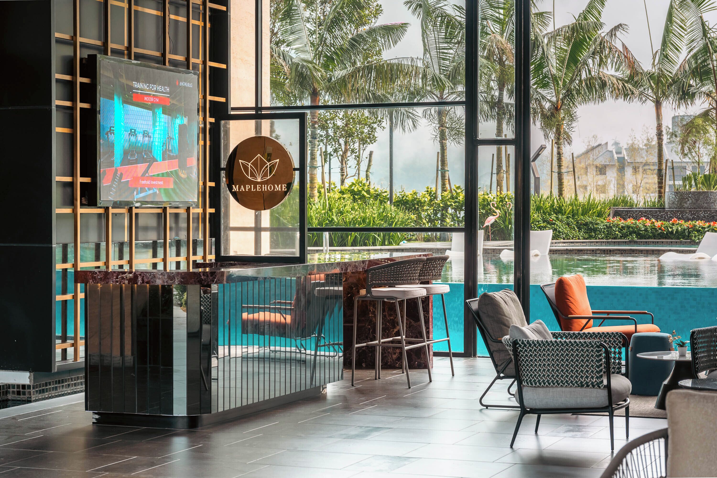 A modern indoor gym with a large screen displaying workout equipment, a logo for 'Maplehome,' and a pool area with lounge chairs and a view of palm trees.