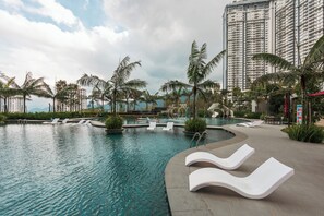 A swimming pool with lounge chairs, palm trees, and high-rise buildings in the background. - Antharas 1 Premier Suites Genting (Genting Highlands)