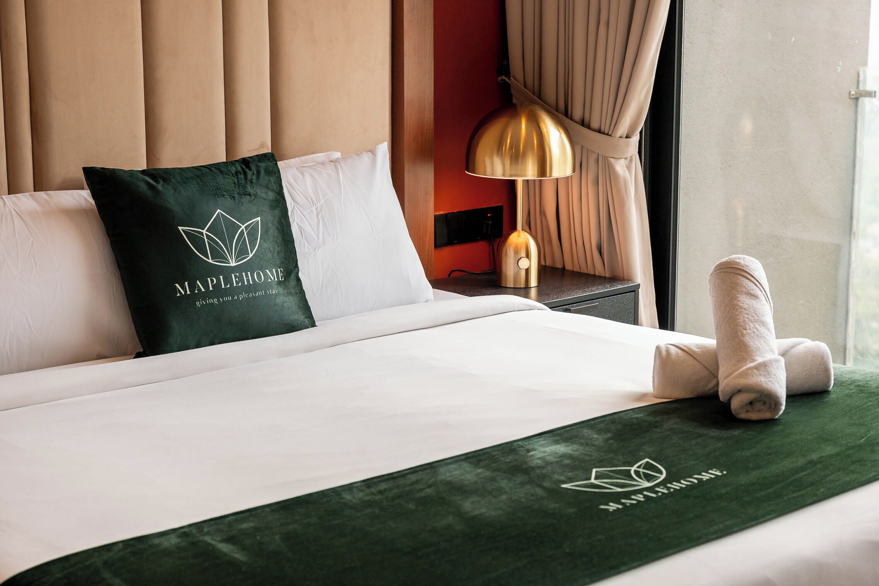 Una camera d'albergo con un letto, un cuscino con un logo, una lampada e un asciugamano.