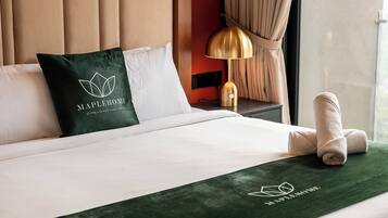 Una camera d'albergo con un letto, un cuscino con un logo, una lampada e un asciugamano.