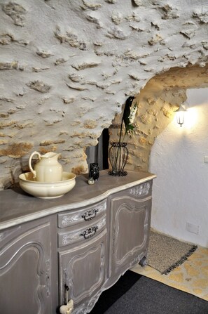 A stone wall, a white cabinet with drawers, a vase with flowers, and a wall-mounted light fixture. - L' Atelier (Cornillon)