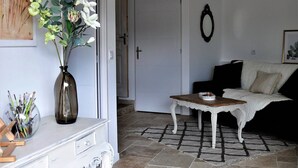 Ett rum med ett vitt konsolbord, en vas med blommor, en vit soffa och en dörr som leder till ett annat rum.