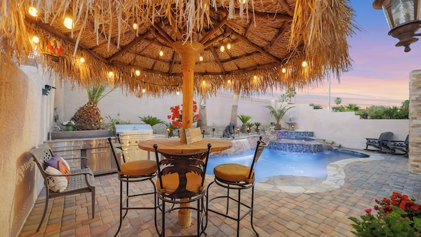 An outdoor patio with a thatched umbrella, a pool, and a grill.