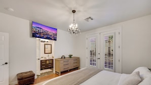 A bedroom with a bed, a dresser, a television, and a chandelier.