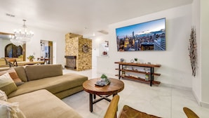 A modern living room with a large flat-screen TV, a stone accent wall, a chandelier, and a wooden coffee table.
