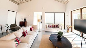 Un salon spacieux avec un plafond haut, une grande fenêtre, un ensemble de canapés, une table basse et un téléviseur.