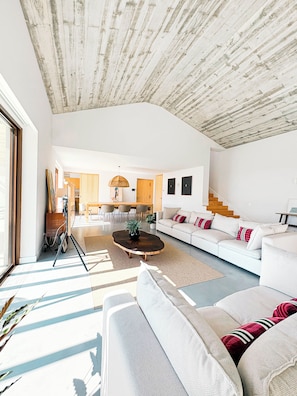 A spacious living room with a white sofa, a coffee table, and a dining area in the background.