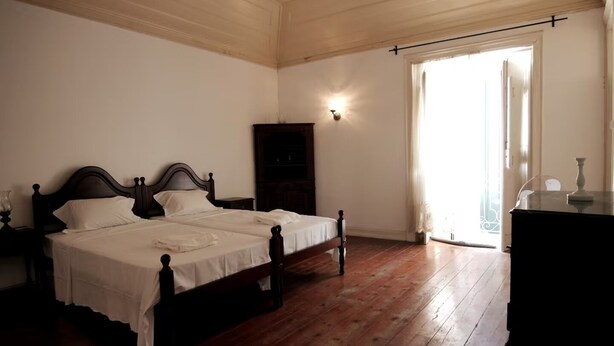 Un dormitorio con dos camas, un tocador, una mesita de noche, una lámpara de pared y un ventanal grande.