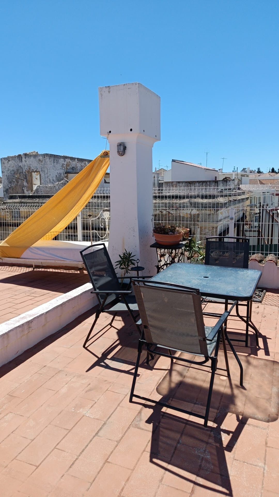Una terraza en la azotea con una mesa, sillas, un tobogán amarillo y una columna blanca.
