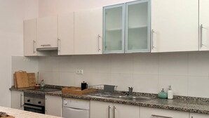 Una cocina con armarios blancos, encimera de granito, mesa de comedor de madera con mantel estampado y una lámpara colgante.
