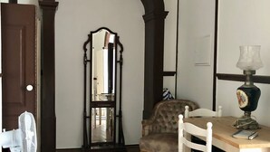 Una habitación con suelo de madera, una mesa de comedor con sillas, un espejo, un ventilador y una lámpara.