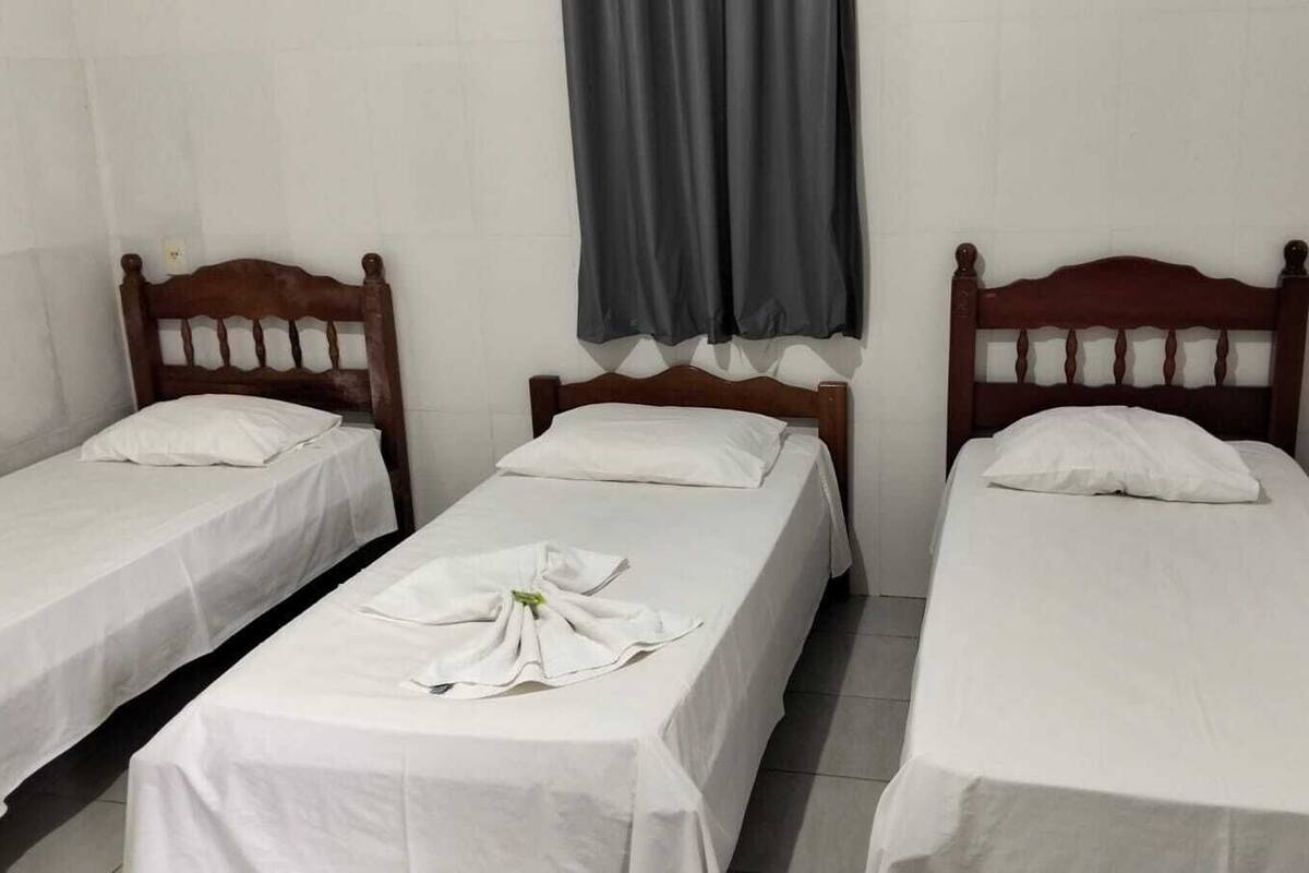 Una habitación con tres camas individuales, cada una con cabecero de madera y ropa de cama blanca.
