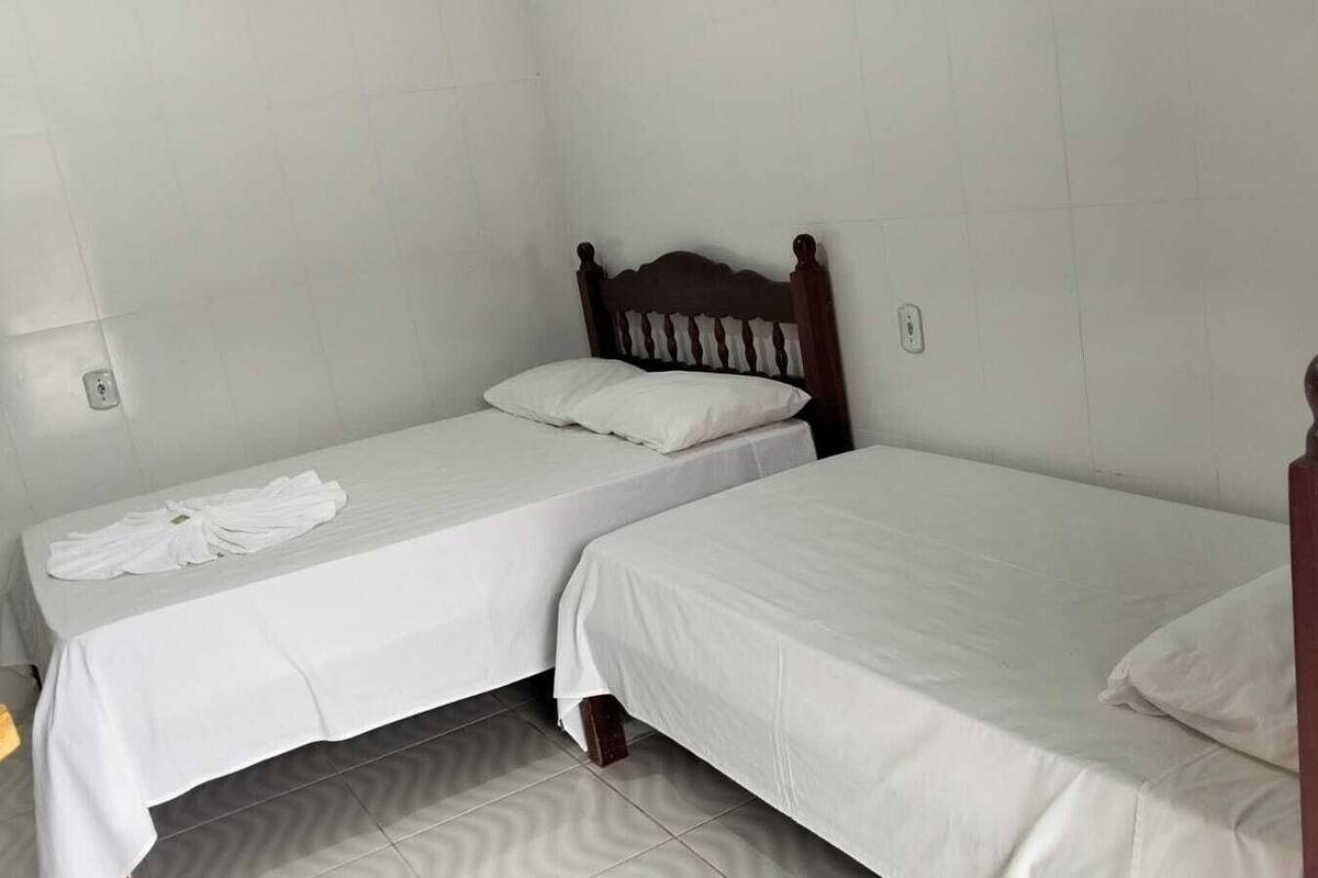 Una habitación pequeña y limpia con dos camas individuales, un cabecero de madera y una pared de azulejos blancos.