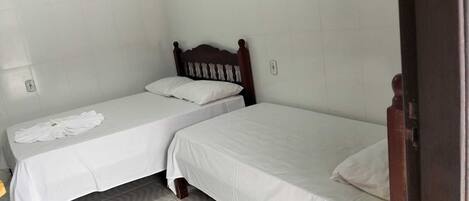 Une petite chambre propre, avec deux lits simples, une tête de lit en bois et un mur recouvert de carreaux blancs.