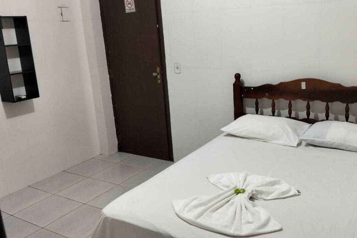 Una cama individual con cabecera de madera, una colcha blanca y dos almohadas. Una toalla doblada está sobre la cama.