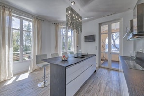 A modern kitchen with a central island, large windows, and a chandelier. - Villa les Romarins at the port of Santa Lucia by Sea View Property Rental (Saint-Raphaël)