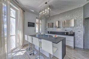 A modern kitchen with a central island, bar stools, a chandelier, and a large window with curtains. - Villa les Romarins at the port of Santa Lucia by Sea View Property Rental (Saint-Raphaël)