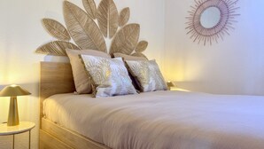 Un lit avec une tête de lit ornée d’un motif de feuilles, un miroir rond fixé au mur et deux lampes de chevet.