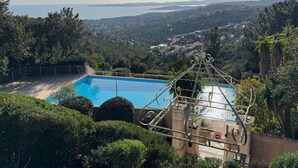 A swimming pool with a view of a coastal landscape, surrounded by greenery and a decorative metal fence.