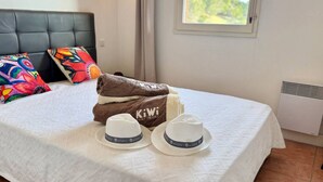 A bed with a white bedspread, two white hats, and a brown towel with 'KiWi' branding.