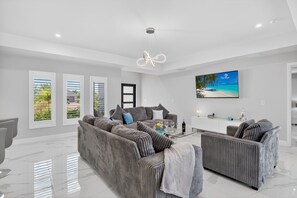 Ein modernes Wohnzimmer mit einem großen grauen Sofa, einem Glastisch und einem Gemälde, das eine Strandansicht zeigt.