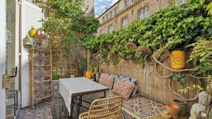Une terrasse extérieure avec une table et des chaises, un tapis à motifs et une clôture en bambou.