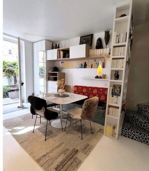 Ein modernes Wohnzimmer mit einem Esstisch, zwei Stühlen, einem Bücherregal und einer Wand mit rotem Muster.